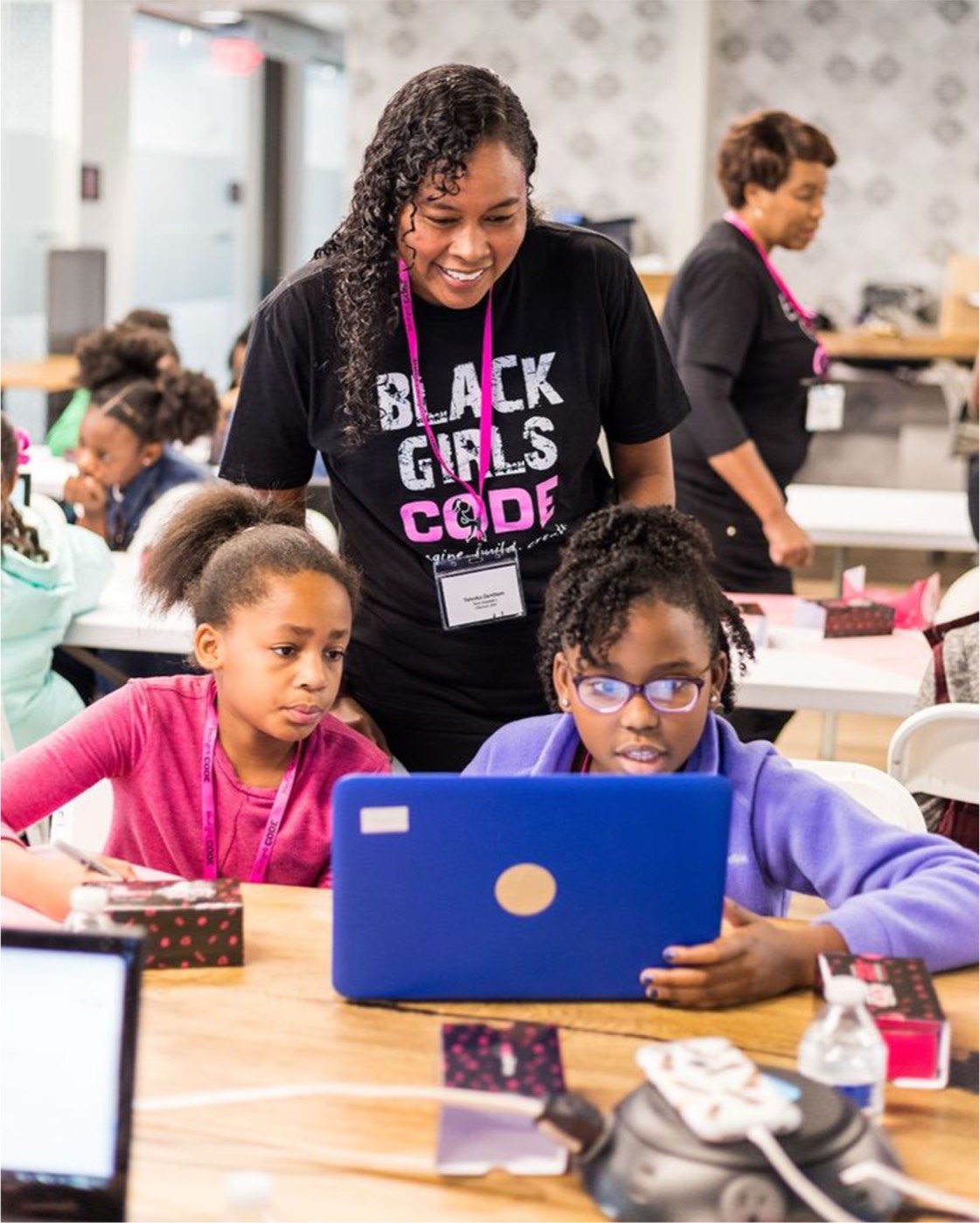An instructor helping two children working on laptops at a coding workshop